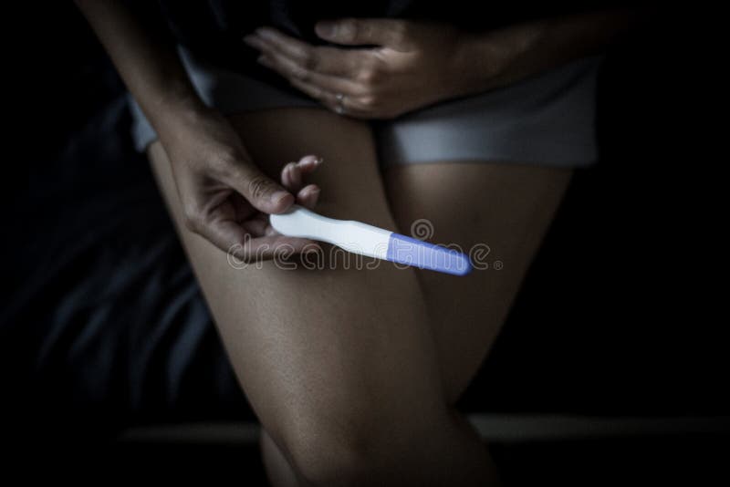 Χέρι γυναικών σχετικά με την κοιλιά της μετά από να εξετάσει τη δοκιμή εγκυμοσύνης στην κρεβατοκάμαρά της, ταινία που τονίζεται στοκ φωτογραφία με δικαίωμα ελεύθερης χρήσης