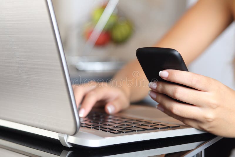Χέρι γυναικών χρησιμοποιώντας ένα έξυπνο τηλέφωνο και δακτυλογραφώντας ένα lap-top στο σπίτι