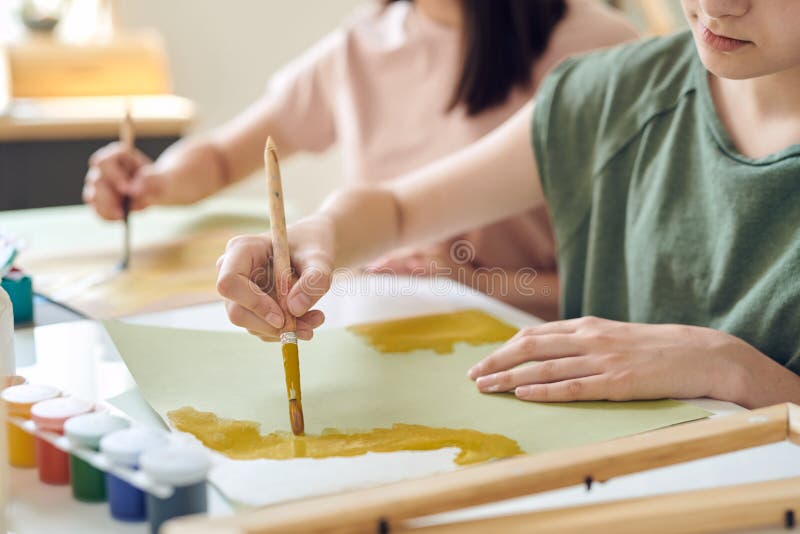χέρια έφηβης μαθήτριας που ζωγραφίζει με κίτρινες γούνες ή χρώμα του νερού σε χαρτί στοκ εικόνες