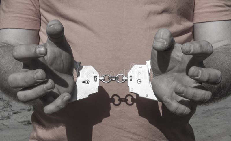 Χέρια ενός βάναυσου ατόμου στις χειροπέδες πίσω από την πλάτη του σε μια πορτοκαλιά μπλούζα Εγκληματική τιμωρία της φυλάκισης στη στοκ φωτογραφία με δικαίωμα ελεύθερης χρήσης Χέρια ενός βάναυσου ατόμου στις χειροπέδες πίσω από την πλάτη του σε μια πορτοκαλιά μπλούζα Εγκληματική τιμωρία της φυλάκισης στη στοκ φωτογραφία με δικαίωμα ελεύθερης χρήσης