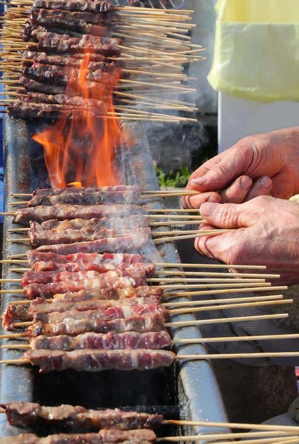 χέρια σεφ και αναλαμπή της φωτιάς και των σκιών κρέατος που ονομάζονται ARROSTICINI και είναι ιταλικό πιάτο στοκ φωτογραφία