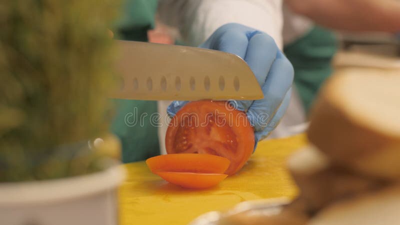 Χέρια του μάγειρα που χρησιμοποιεί το μαχαίρι για την τέμνουσα ντομάτα στις φέτες και τα κομμάτια κύκλων στο εστιατόριο στοκ φωτογραφίες Χέρια του μάγειρα που χρησιμοποιεί το μαχαίρι για την τέμνουσα ντομάτα στις φέτες και τα κομμάτια κύκλων στο εστιατόριο στοκ φωτογραφίες