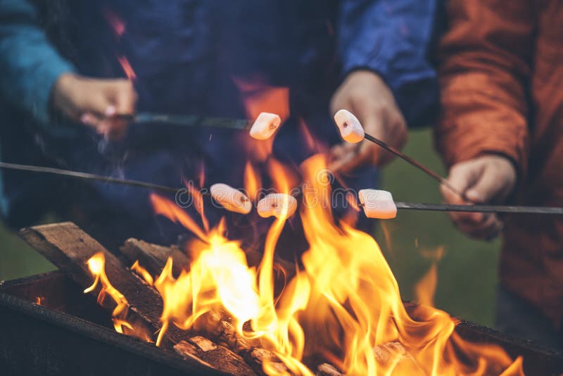 Χέρια των φίλων που ψήνουν marshmallows πέρα από την πυρκαγιά σε μια σχάρα