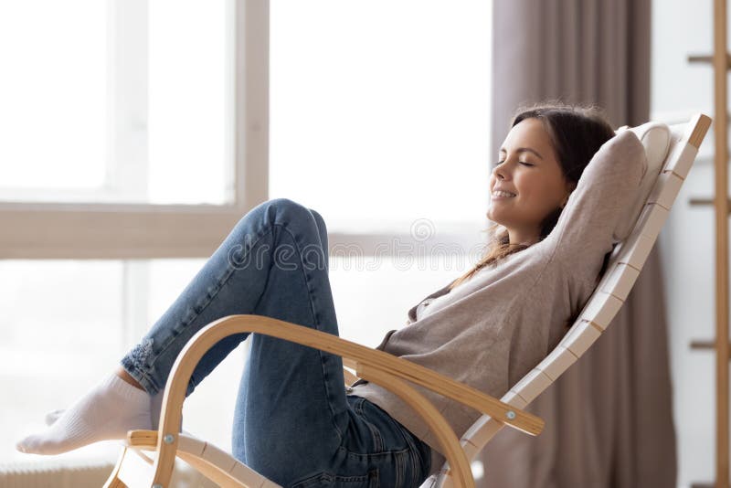 Relaxed calm young woman lounging sitting in comfortable wooden rocking chair breathing fresh air dreaming, happy lazy girl chilling relaxing enjoying no stress free peaceful quiet weekend at home. Relaxed calm young woman lounging sitting in comfortable wooden rocking chair breathing fresh air dreaming, happy lazy girl chilling relaxing enjoying no stress free peaceful quiet weekend at home