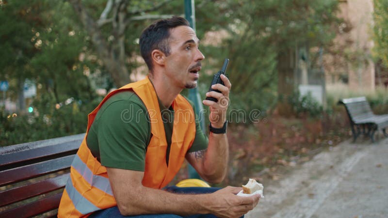 χαλαρός ανάδοχος απαντώντας στο walkietalkie στην πόλη κλείσιμο. άντρας που κρατά σάντουιτς στοκ εικόνα με δικαίωμα ελεύθερης χρήσης