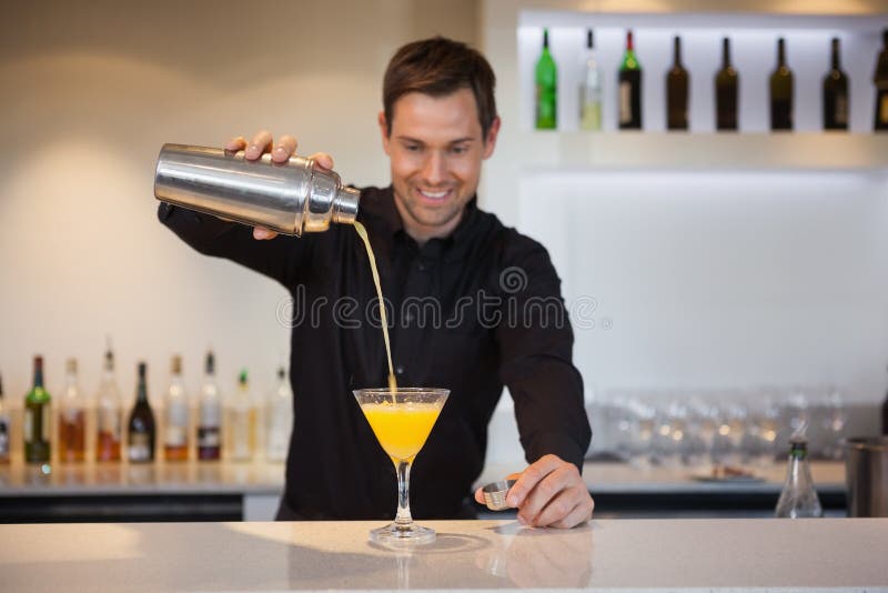 Χαμογελώντας bartender που χύνει το κίτρινο κοκτέιλ στο γυαλί στοκ εικόνες Χαμογελώντας bartender που χύνει το κίτρινο κοκτέιλ στο γυαλί στοκ εικόνες