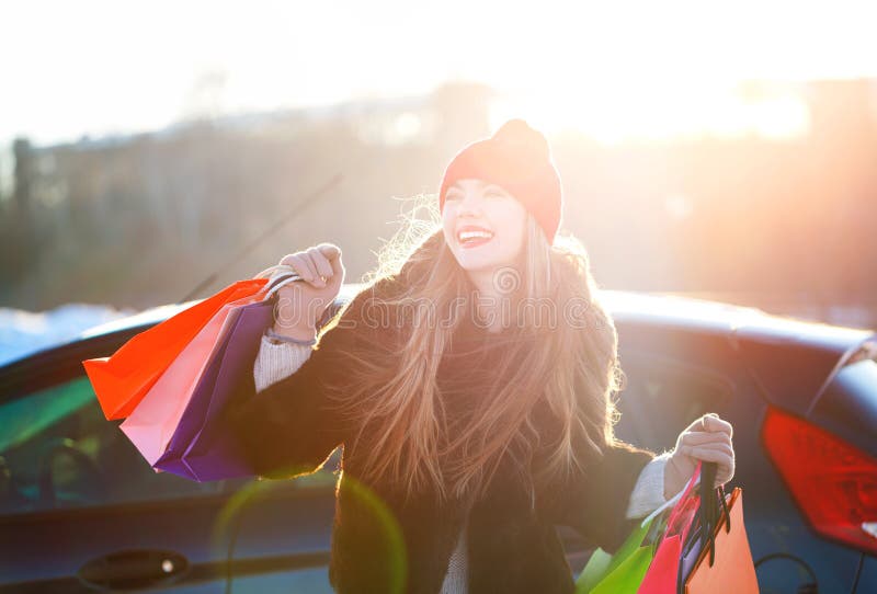 Χαμογελώντας καυκάσια γυναίκα που κρατά την τσάντα αγορών της κοντά στο αυτοκίνητο