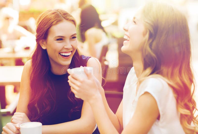 Communication and friendship concept - smiling young women with coffee cups at cafe. Communication and friendship concept - smiling young women with coffee cups at cafe