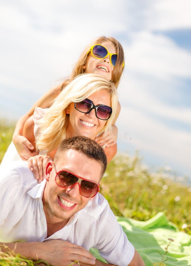 Summer holidays, family, child and happy people concept - smiling family in sunglasses lying on blanket outdoors. Summer holidays, family, child and happy people concept - smiling family in sunglasses lying on blanket outdoors