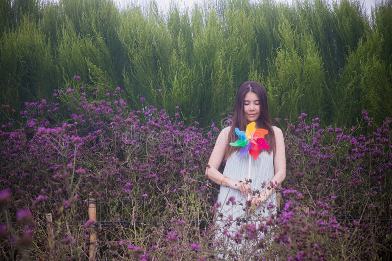 Χαμογελαστή γυναίκα που κρατά ανεμόμυλους ουράνιου τόξου στον κήπο με λερβένα