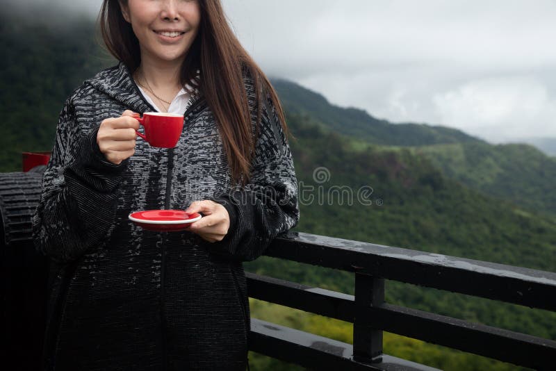 Χαμογελαστή νεαρή ασιάτισσα που πίνει ζεστό καφέ σε θέα σκηνικού το πρωί, μπροστά