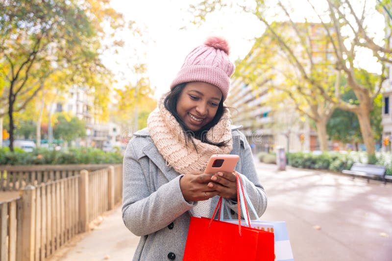 Cute latin woman standing holding shopping bags, browsing smartphone apps shopping online. Cute latin woman standing holding shopping bags, browsing smartphone apps shopping online