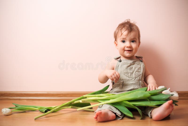 Smiling baby boy 2 years old posing with a bouquet of white tulips over pink colored background. Boy sitting with a flowers. funny boy with bouquet of flowers. Happy mothers day. Happy womans day. Smiling baby boy 2 years old posing with a bouquet of white tulips over pink colored background. Boy sitting with a flowers. funny boy with bouquet of flowers. Happy mothers day. Happy womans day
