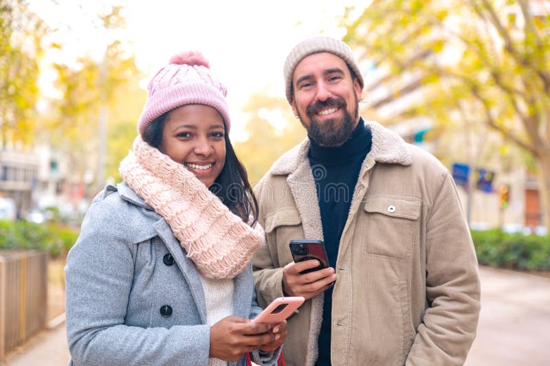 Cute multiethnic couple of man and woman standing holding shopping bags, browsing smartphone apps shopping online looking at camera. Cute multiethnic couple of man and woman standing holding shopping bags, browsing smartphone apps shopping online looking at camera