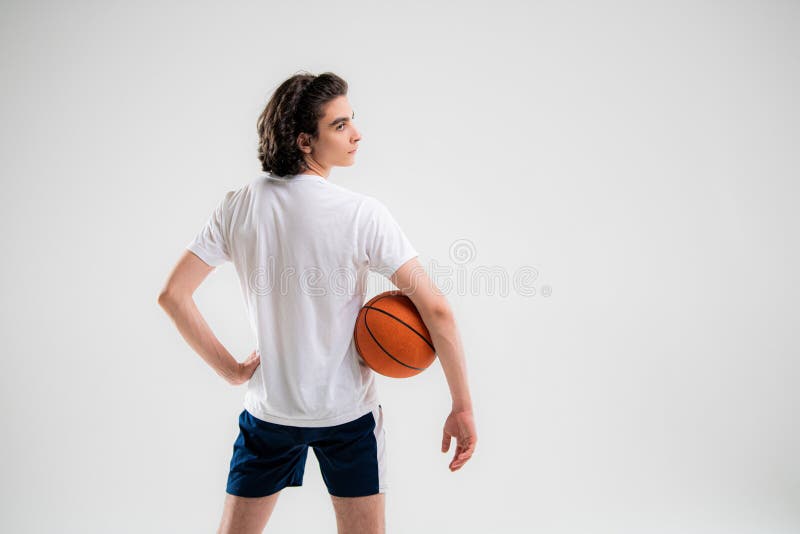 χαμογελαστός έφηβος μπασκετμπολίστας ποζάροντας με μια μπάλα στο χέρι σε λευκό φόντο
