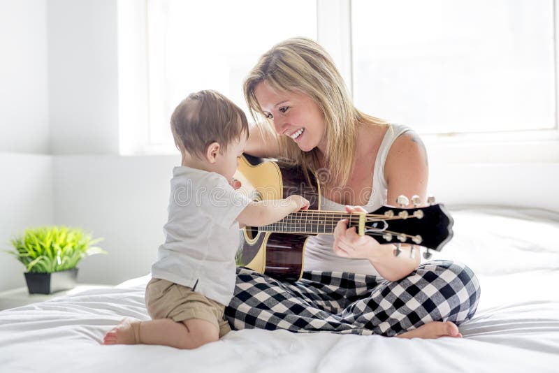 Χαμογελώντας γυναίκα με τη συνεδρίαση κιθάρων στο κρεβάτι με το παιδί