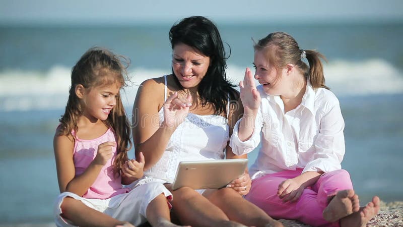 Χαμογελώντας μητέρα και κόρες που χρησιμοποιούν την ταμπλέτα στην παραλία