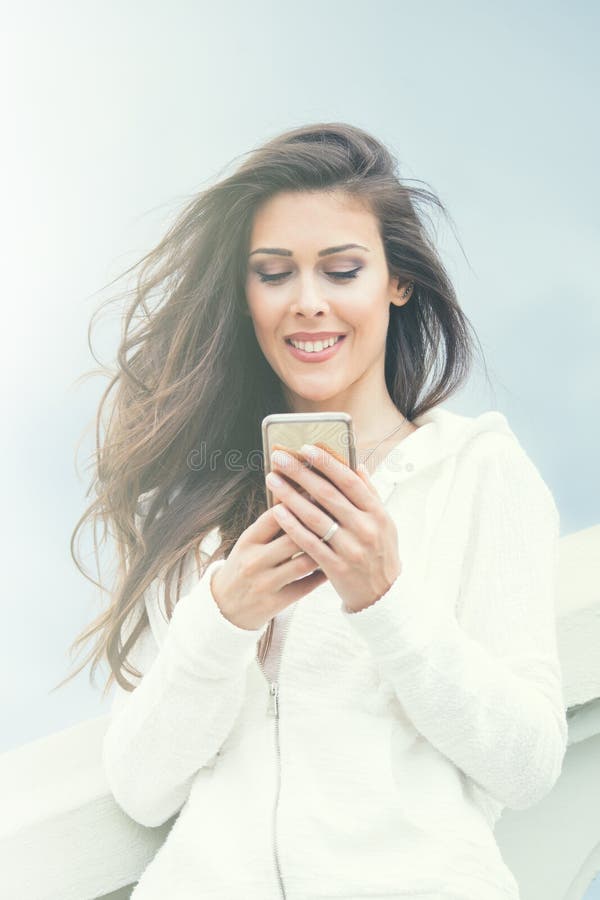 Χαμογελώντας νέο αστικό κορίτσι με το smartphone στην άσπρη θερινή ημέρα πουλόβερ στην πόλη στοκ φωτογραφίες