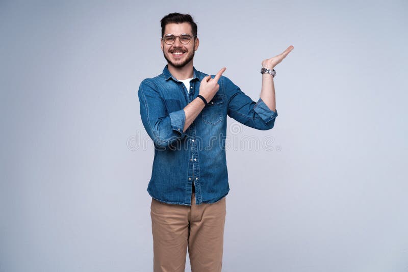 Χαμογελώντας νέο περιστασιακό άτομο που παρουσιάζει κάτι στο γκρίζο υπόβαθρο στοκ εικόνα Χαμογελώντας νέο περιστασιακό άτομο που παρουσιάζει κάτι στο γκρίζο υπόβαθρο στοκ εικόνα
