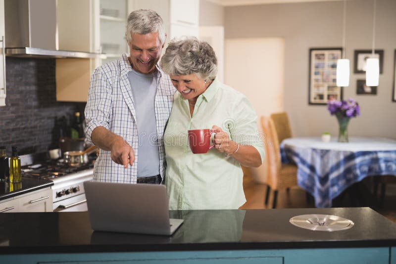 Χαμόγελο του ανώτερου lap-top προσοχής ζευγών στεμένος στην κουζίνα στοκ εικόνες Χαμόγελο του ανώτερου lap-top προσοχής ζευγών στεμένος στην κουζίνα στοκ εικόνες