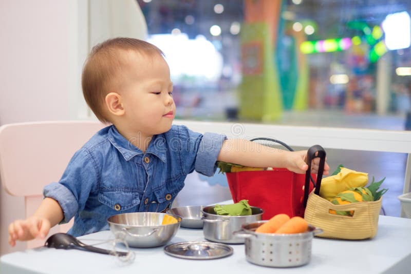 Cute little Asian 18 months / 1 year old toddler baby boy child having fun playing alone with cooking toys at play school / child care in department store, Educational toys for young children concept. Cute little Asian 18 months / 1 year old toddler baby boy child having fun playing alone with cooking toys at play school / child care in department store, Educational toys for young children concept