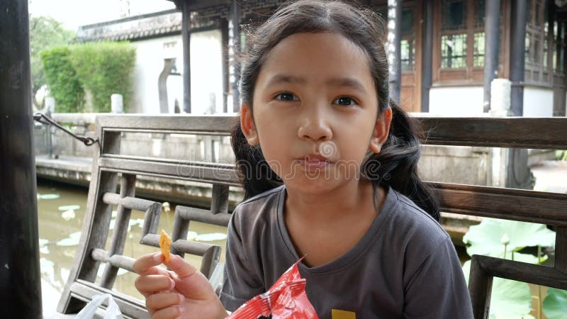 Χαριτωμένο ασιατικό μικρό κορίτσι που τρώει το πρόχειρο φαγητό με την ευτυχία