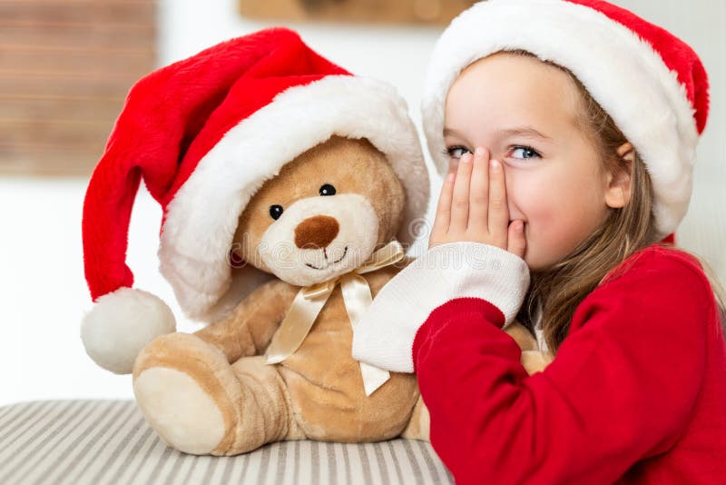 Χαριτωμένο νέο κορίτσι που φορά το καπέλο santa που ψιθυρίζει ένα μυστικό στο teddy παιχνίδι χριστουγεννιάτικου δώρου αρκούδων τη στοκ εικόνα με δικαίωμα ελεύθερης χρήσης