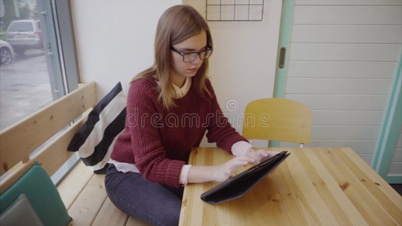 Χαριτωμένος νέος σπουδαστής γυναικών με την ταμπλέτα στον καφέ