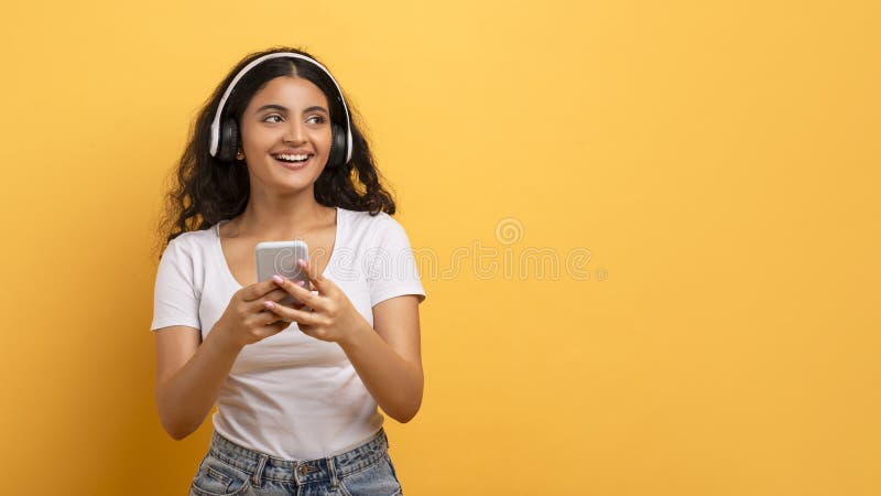 A content young lady interacts with a smartphone while wearing headphones, indicating the digital lifestyle. A content young lady interacts with a smartphone while wearing headphones, indicating the digital lifestyle