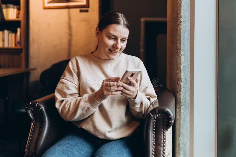 30s woman laughing holding smartphone, enjoying doing online ecommerce shopping in mobile apps or watching video at home. 30s woman laughing holding smartphone, enjoying doing online ecommerce shopping in mobile apps or watching video at home