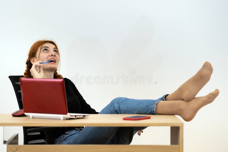 χαρούμενη νεαρή εργαζόμενη στο γραφείο που κάθεται χαλαρή με τα πόδια στο τραπέζι πίσω από το γραφείο εργασίας με το κινητό του φο στοκ εικόνες