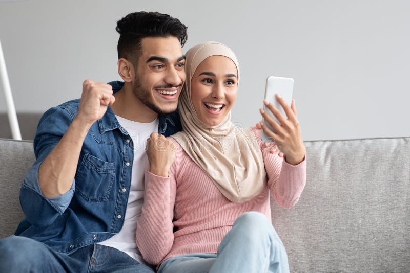 χαρούμενο αραβικό ζευγάρι με smartphone που σηκώνει γροθιές στοκ εικόνες
