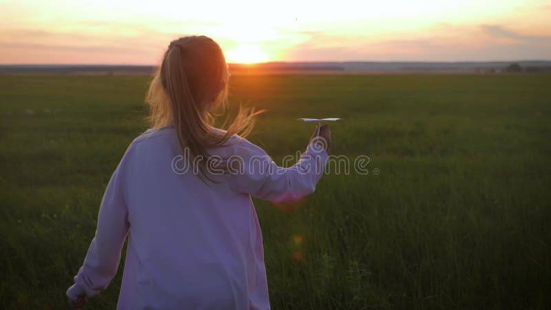 Χαρούμενο κοριτσάκι που παίζει με ένα χάρτινο αεροπλάνο έξω κατά τη διάρκεια του ηλιοβασίλεμα Ιδέα ενός μεγάλου παιδικού ονείρου