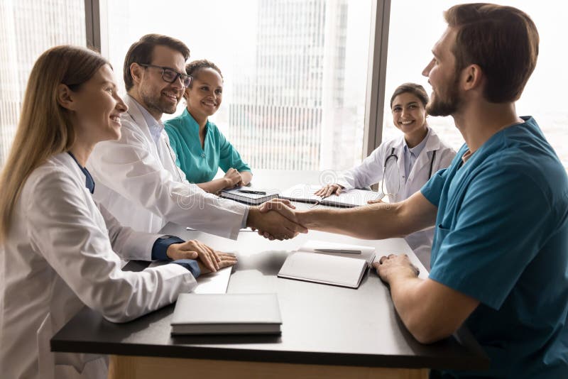Χαρούμενοι νεαροί γιατροί χειρουργοί-θεραπευτές κάνουν χειραψία σε συνέδριο του προσωπικού στοκ εικόνα