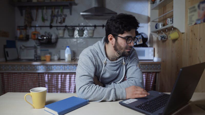 χαρούμενος νεαρός επιχειρηματίας που εργάζεται σε φορητό υπολογιστή στην κουζίνα το βράδυ στοκ φωτογραφία