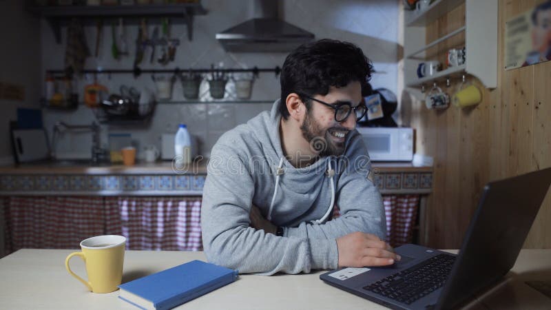 χαρούμενος νεαρός επιχειρηματίας που εργάζεται σε φορητό υπολογιστή στην κουζίνα το βράδυ στοκ εικόνες