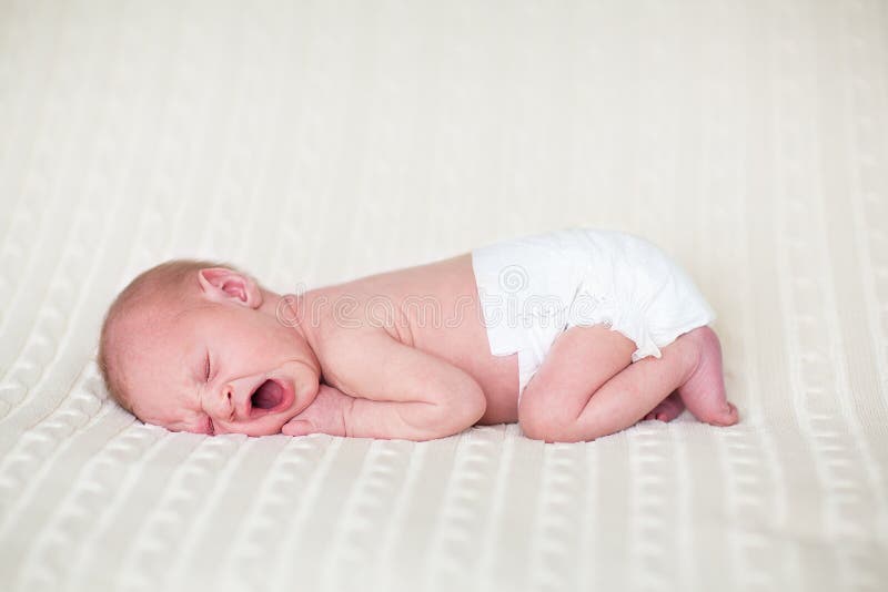 Tiny yawning newborn baby in a diaper sleeping on a knitted blanket. Tiny yawning newborn baby in a diaper sleeping on a knitted blanket