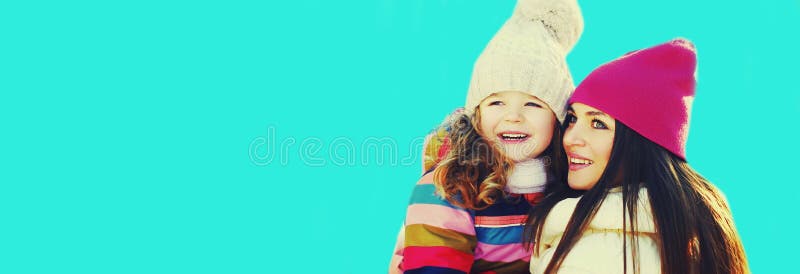 χειμωνιάτικο πορτρέτο της ευτυχισμένης χαμογελαστής μητέρας και του μικρού κοριτσιού που κοιτούν μακριά στο μπλε φόντο