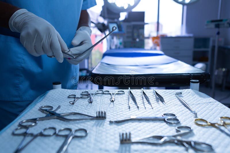 Mid section close-up of African-american surgeon holding surgical instrument in operating room at hospital. Shot in real medical hospital with doctors nurses and surgeons in authentic setting. Mid section close-up of African-american surgeon holding surgical instrument in operating room at hospital. Shot in real medical hospital with doctors nurses and surgeons in authentic setting