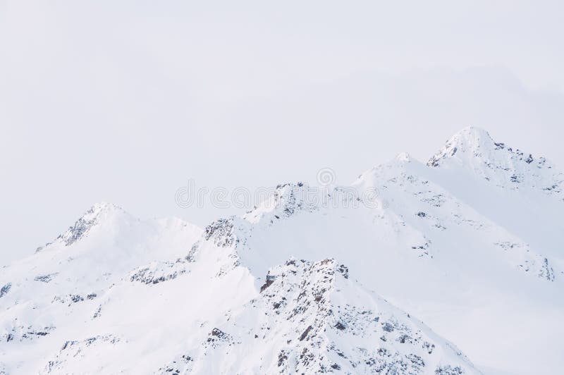 Snow-covered mountain peaks against the cloudy sky. Beautiful winter landscape. Caucasus mountains, Elbrus region, Russia. Snow-covered mountain peaks against the cloudy sky. Beautiful winter landscape. Caucasus mountains, Elbrus region, Russia