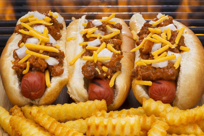 Three chili hot dogs with cheese and onions in buns Grilled with French fries and a hot flaming barbecue grill. Three chili hot dogs with cheese and onions in buns Grilled with French fries and a hot flaming barbecue grill.