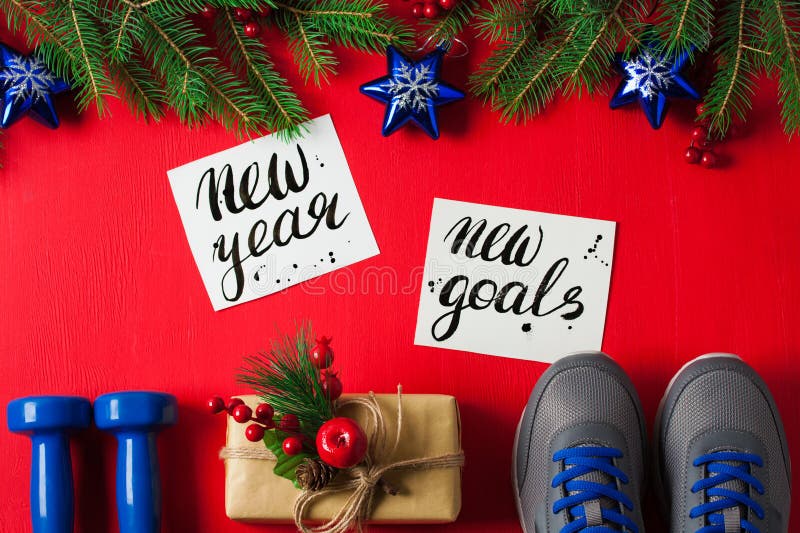 Christmas sport flat lay composition blue dumbbells sneakers gift box spruce tree branches new nnnyear new goals lettering red wooden background. Concept new year special for healthy lifestyle nnnand sport. Christmas sport flat lay composition blue dumbbells sneakers gift box spruce tree branches new nnnyear new goals lettering red wooden background. Concept new year special for healthy lifestyle nnnand sport