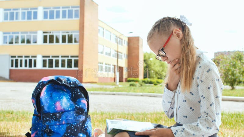 11 year old schoolgirl reads a book while sitting on the grass on the grass near the school. 11 year old schoolgirl reads a book while sitting on the grass on the grass near the school