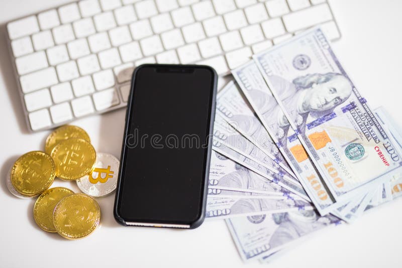 Χρυσά νομίσματα Bitcoin στα τραπεζογραμμάτια δολαρίων Υπόβαθρο γραφείων Άσπρο πληκτρολόγιο, κινητό τηλέφωνο, και χρήματα Ισορροπί στοκ εικόνα Χρυσά νομίσματα Bitcoin στα τραπεζογραμμάτια δολαρίων Υπόβαθρο γραφείων Άσπρο πληκτρολόγιο, κινητό τηλέφωνο, και χρήματα Ισορροπί στοκ εικόνα