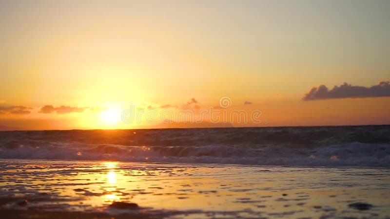 Χρυσό ηλιοβασίλεμα με τα κύματα στην παραλία
