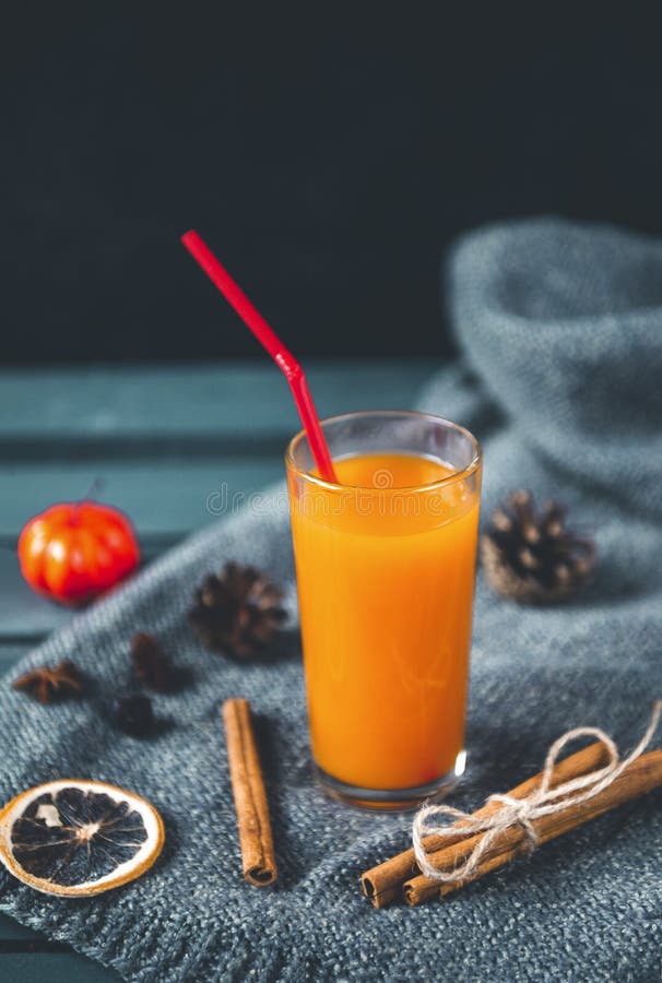 1 Cup orange vegetable pumpkin juice with a straw, cinnamon, cones, cinnamon, a slice of dried orange on a dark background. 1 Cup orange vegetable pumpkin juice with a straw, cinnamon, cones, cinnamon, a slice of dried orange on a dark background