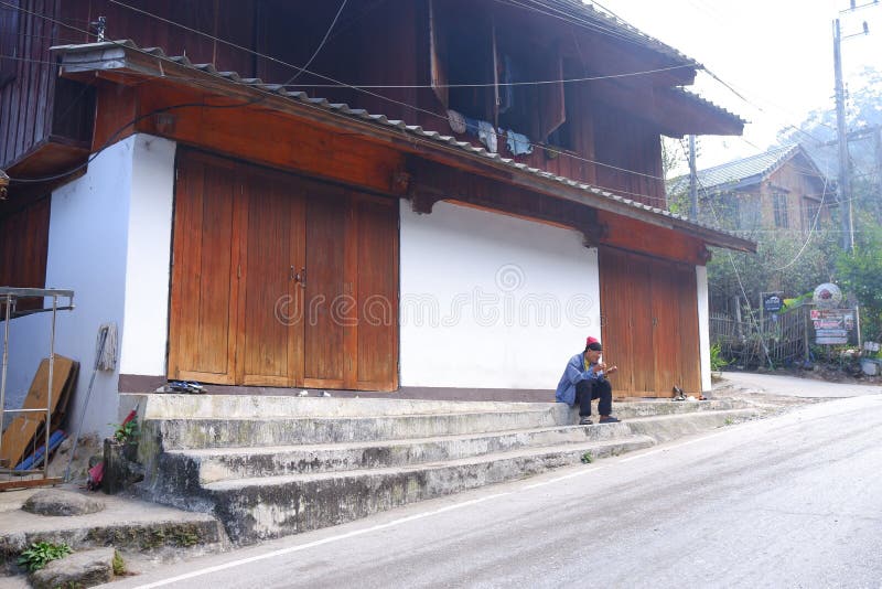 A local villager sits in front of an old Thai traditional wooden house next to the road in Mae Kampong, Chiangmai, Thailand. A local villager sits in front of an old Thai traditional wooden house next to the road in Mae Kampong, Chiangmai, Thailand.