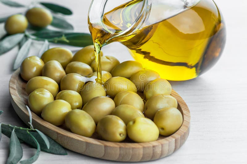 Χύνοντας ελαιόλαδο από το μπουκάλι στο γυαλί στις ακατέργαστες τουρκικές πράσινες ελιές στο κύπελλο μπαμπού στοκ εικόνες Χύνοντας ελαιόλαδο από το μπουκάλι στο γυαλί στις ακατέργαστες τουρκικές πράσινες ελιές στο κύπελλο μπαμπού στοκ εικόνες