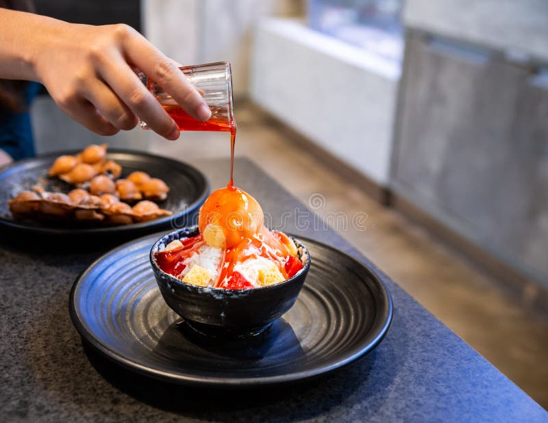 Χύνοντας σάλτσα φραουλών χεριών σε Bingsu, ένα κορεατικό ξυρισμένο επιδόρπιο πάγου με τα γλυκά καλύμματα όπως το παγωτό βανίλιας στοκ φωτογραφία