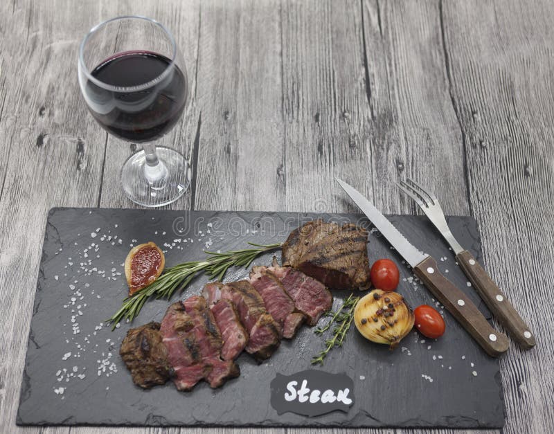 Ψημένη στη σχάρα striploin μπριζόλα σε ένα πιάτο πετρών με ένα ποτήρι του κόκκινου κρασιού με ένα δίκρανο και ένα μαχαίρι στοκ εικόνες με δικαίωμα ελεύθερης χρήσης Ψημένη στη σχάρα striploin μπριζόλα σε ένα πιάτο πετρών με ένα ποτήρι του κόκκινου κρασιού με ένα δίκρανο και ένα μαχαίρι στοκ εικόνες με δικαίωμα ελεύθερης χρήσης